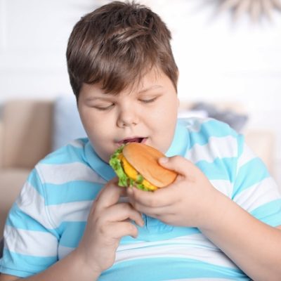 Boy with obesity eating a burger.