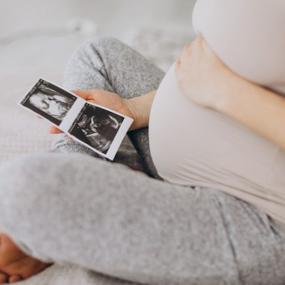 Pregnant woman with ultrasound photo sitting on bed