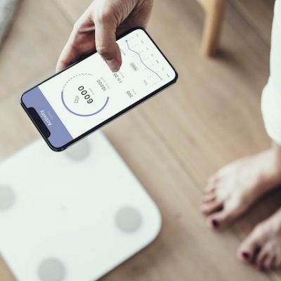 Woman using digital health platform on her phone standing next to scales.