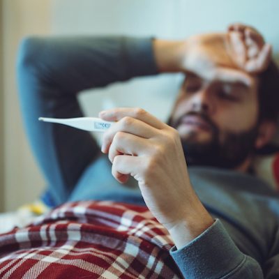 Man staying in bed measuring temperature feeling sick