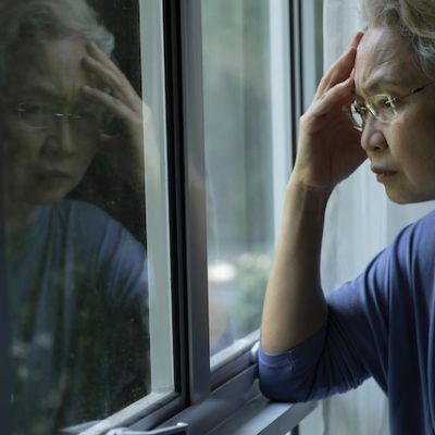 Sad and worried senior woman looking through window