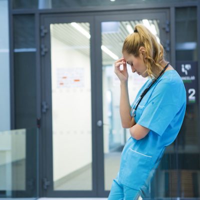 Upset female doctor standing in corridor.
