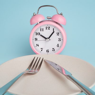 Alarm clock and plate with cutlery. Concept of intermittent fasting, lunchtime, diet and weight loss