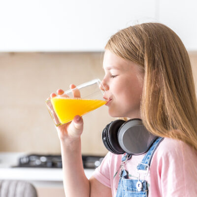 Girl with headphones drinking orange juice in the kitchen