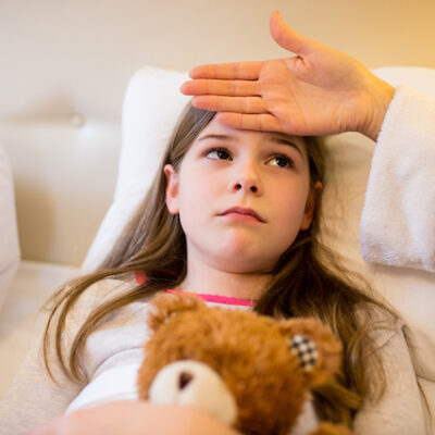 Mother checking fever of her daughter in bedroom.