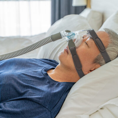 Middle age man wearing CPAP mask and headgear to help with his sleep apnea while sleeping in his bed