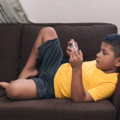 Child lying on a couch looking at a smart phone.