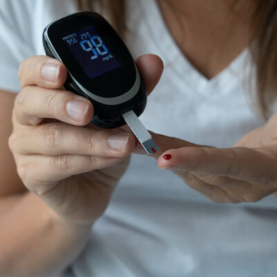 Close up of woman measuring blood sugar level with Continuous Glucose Monitor (CGM).