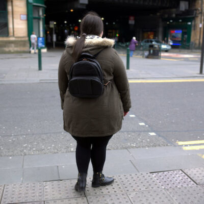 Woman standing at pedestrian crossing in the UK.