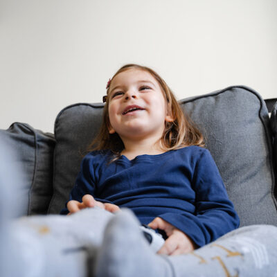 Toddler girl playing video game console at home in living room on the sofa.