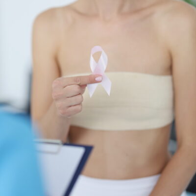 Woman holds pink ribbon in her hand during breast examination at doctor appointment.