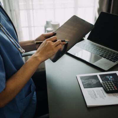 Young doctor with diary sitting at desk in medical clinic