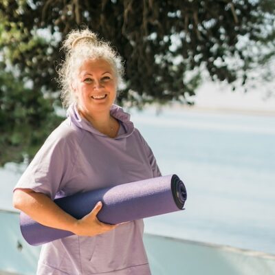 Elderly woman with grey hair holding a yoga mat.