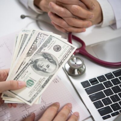Patient giving money to medical doctor in hospital setting.