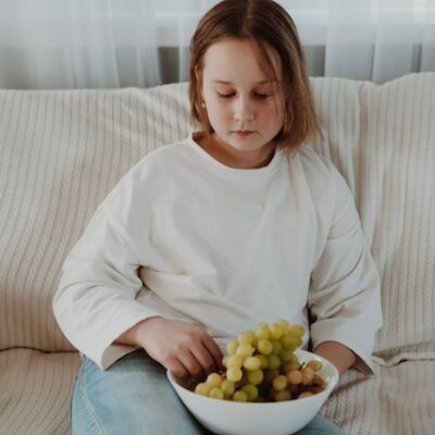 A girl eating grapes on the couch.