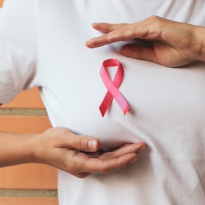 Woman with pink awareness ribbon against brick wall background.