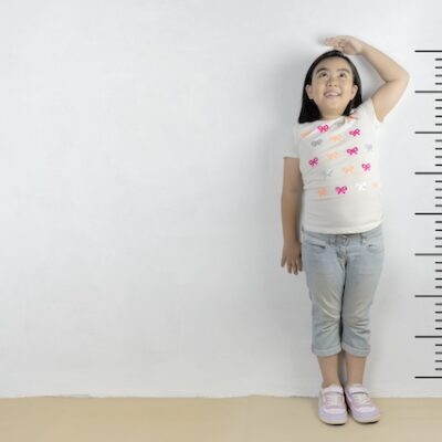 Young girl stands against a wall having her height measured.