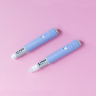 Two Ozempic pens against a pink background.