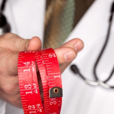 Doctor with stethoscope holding red measuring tape.