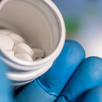 Person wearing gloves holding a bottle of pills.