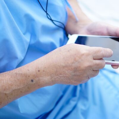 Elderly hospital patient using a smartphone.