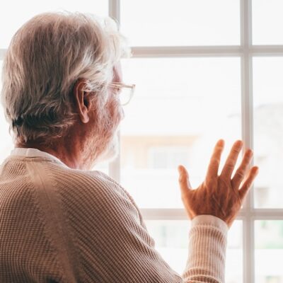 Back view of an elderly man looking out of a window.