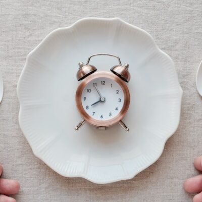 Hands holding fork and spoon and a clock on the plate, Intermittent fasting diet concept.