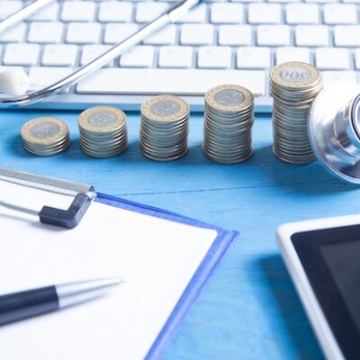 Stethoscope, tablet, computer keyboard, and coins on the blue background.