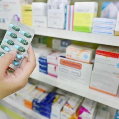 Hand holding pills in a pharmacy setting.