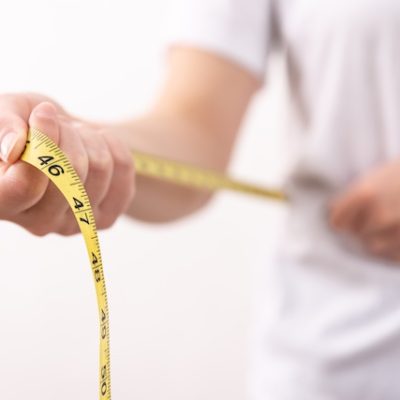 A woman in a white t-shirt holds a yellow centimetre tape in her hands. The concept of losing weight, gaining weight.