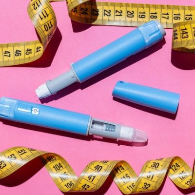 Ozempic pens and a yellow measurement tape on a pink background.