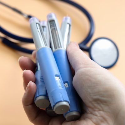 Women's hand holding three blue ozempic injection pens.