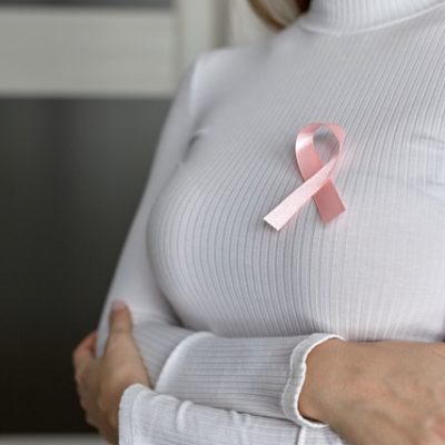 A woman in a white sweater with a pink ribbon in support of breast cancer patients.