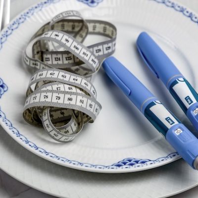 Ozempic pens with a tape measure on a white plate.