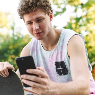 Teenager holding a smartphone and a skateboard.