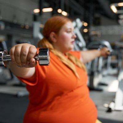 Portrait of young woman with overweight lifting dumbbells and working out in a gym.