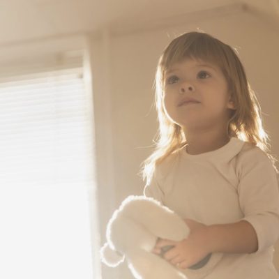 Blonde toddler standing in a bedroom.