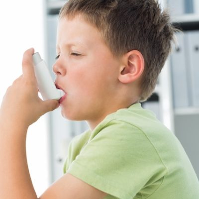 Side view of little boy using an asthma inhaler in clinic.