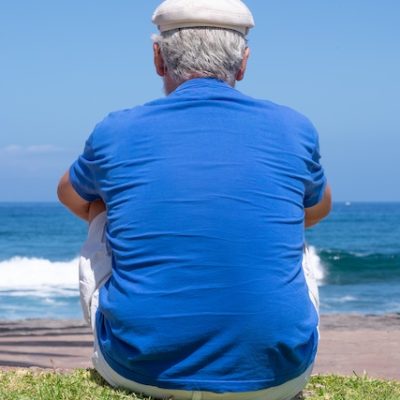 Back view of a man wearing a hat looking at the beach.