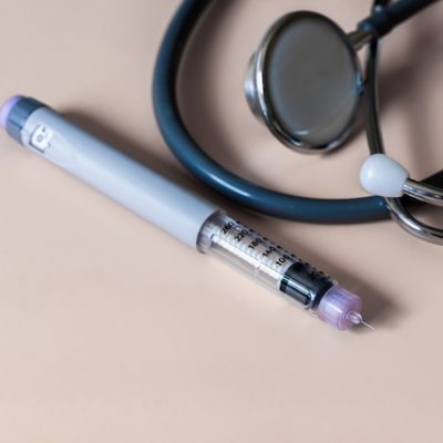 GLP-1 pen and a stethoscopes on a beige table.