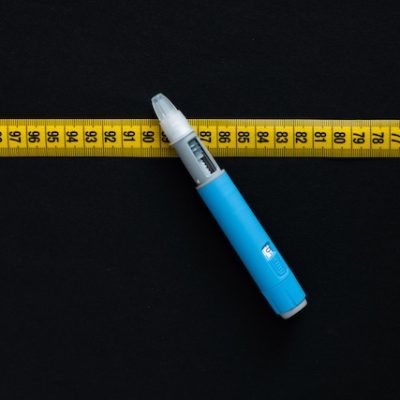 Ozempic pen and a measuring tape on a black background.