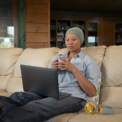 Portrait of a woman with cancer using her laptop on a sofa.