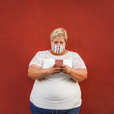 Woman with obesity wearing a mask and using a smartphone.