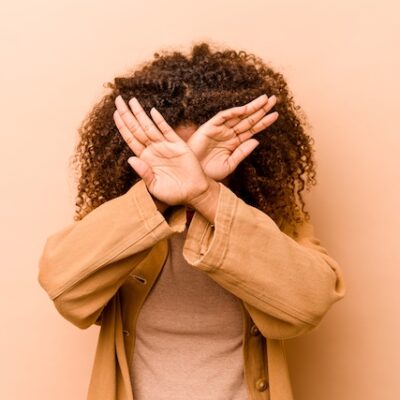 Young woman crossing her arms in front of her face.