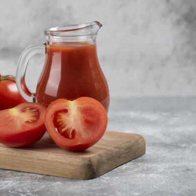 A glass pitcher of tomatoes juice with fresh tomatoes next to it.