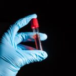 Hand in a medical glove holding a vail of blood.