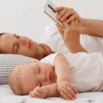 Baby sleeping while mother uses a smartphone.