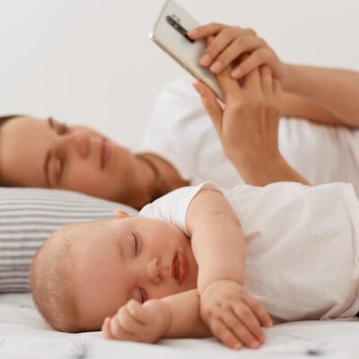 Baby sleeping while mother uses a smartphone.