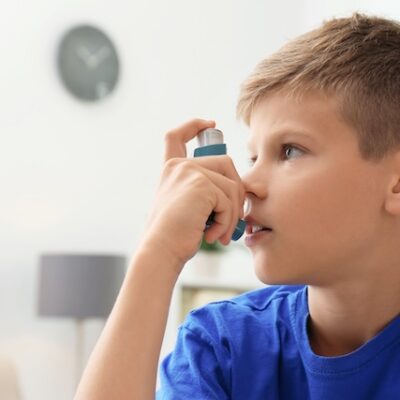 Little boy using asthma inhaler on a blurred background.