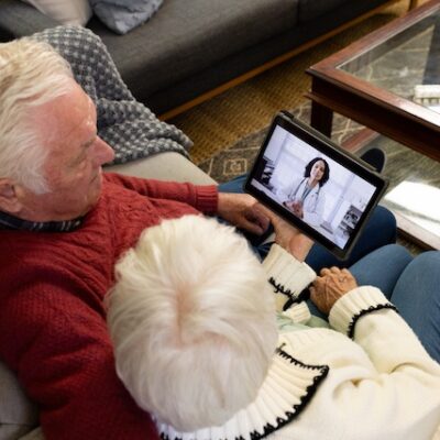 Senior couple having a video call with a doctor in a sunny living room.